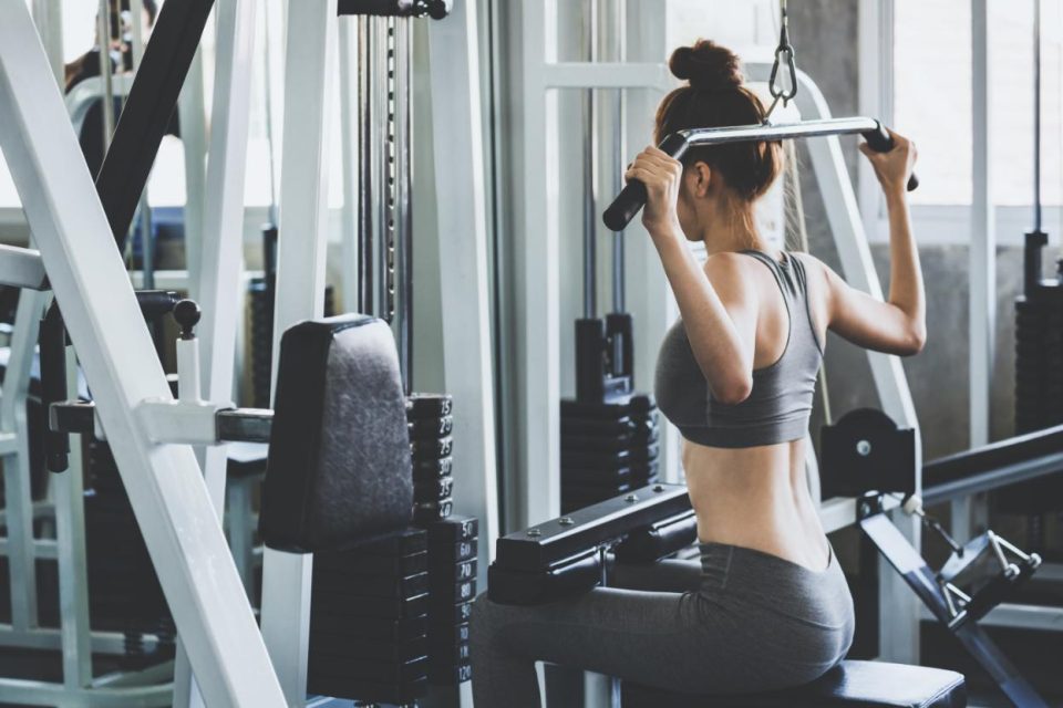 Femme sportive réalisant un lat pulldown avec une machine.